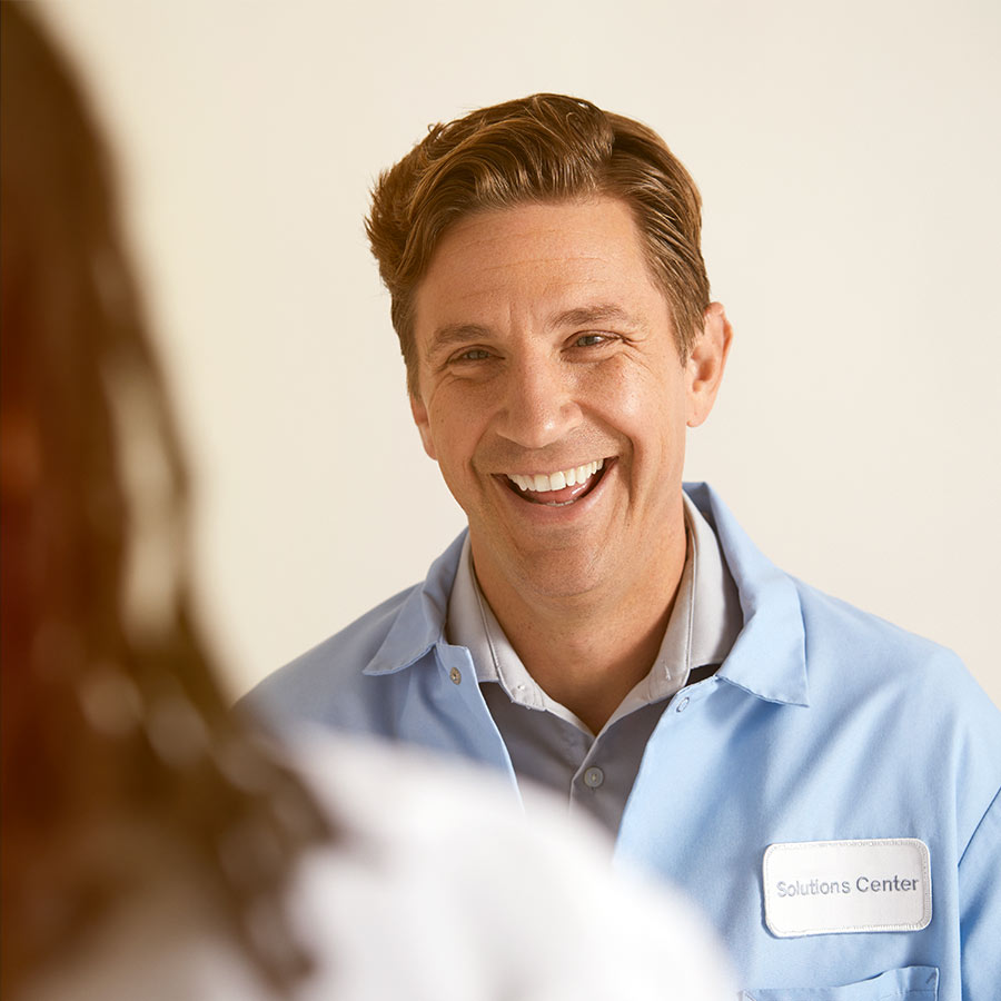 man wearing blue lab coat with a solutions center badge smiling