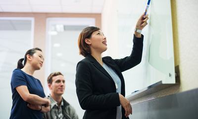 A female leader guiding her fellow employees in a whiteboard discussion.